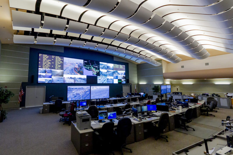 Pictured: A control room, incorporating a video wall display, operator workstations, operator console desks, chairs, and evenly-dispersed low-fatigue room lighting.